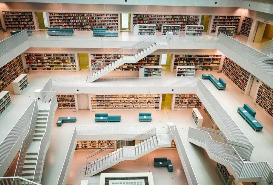 Das Innere der modernen, mehrstöckigen Stadtbibliothek Stuttgart ist mit seinen weißen Wänden und dem minimalistischen Design ein Paradies für Bücherliebhaber. Mehrere Treppen verbinden die Ebenen, die jeweils mit Regalen voller Bücher gesäumt sind. Auf jeder Etage sind grüne Sitzbereiche sichtbar.