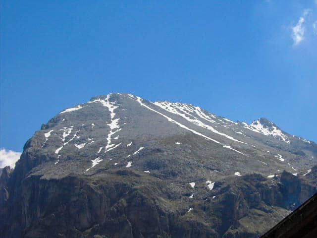 Der majestätische, teilweise mit Schnee bedeckte Berggipfel erhebt sich unter einem klaren, blauen Himmel. Sein zerklüftetes Gelände mit steilen Hängen und felsigen Oberflächen bietet einen anspruchsvollen Aufstieg für diejenigen, die die Schönheit der Natur in der Nähe der Plattkofelhütte genießen möchten.