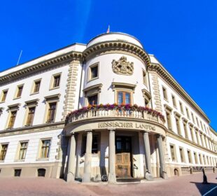 In der Hessischen Landeshauptstadt steht der Hessische Landtag, ein historisches weißes Gebäude mit kunstvollen Details und Bogenfenstern, mit blumengeschmücktem Balkon und blauem Himmel - ein Muss, wenn Sie Wiesbaden entdecken.