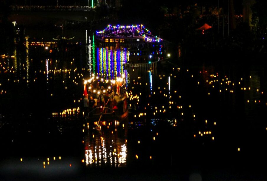 Während der Lichterserenade treiben mit bunten Lichtern geschmückte Boote auf einem nächtlichen Fluss, umgeben von zahlreichen kleinen, leuchtenden Laternen, die sich auf dem Wasser spiegeln und eine festliche und heitere Atmosphäre schaffen.