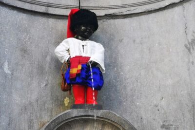 Die Statue eines kleinen Jungen in farbenfroher Tracht und mit Hut, der in einen Brunnen an einer Steinmauer uriniert - Manneken Pis ist eine berühmte Brüsseler Sehenswürdigkeit.
