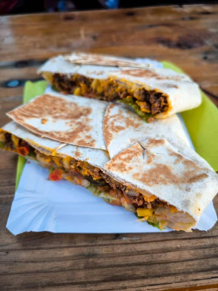 Zwei Hälften eines gegrillten Burritos, gefüllt mit Rindfleisch, Mais und Gemüse, liegen auf einem weißen Tablett, das mit einer grünen Serviette ausgelegt ist. Perfekt, um sie zu genießen, nachdem Sie Wiesbaden entdecken oder an einer der Stadtführungen Wiesbaden teilnehmen.