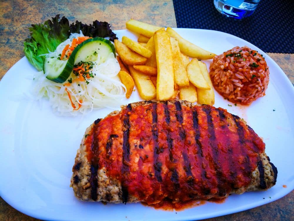Ein Teller mit gegrilltem Hackbraten mit Tomatensoße, dicken Pommes frites, einem Haufen gewürztem Reis und Salatbeilage - so wie in einem der Erfurter Lieblingsrestaurants in der Stadt.