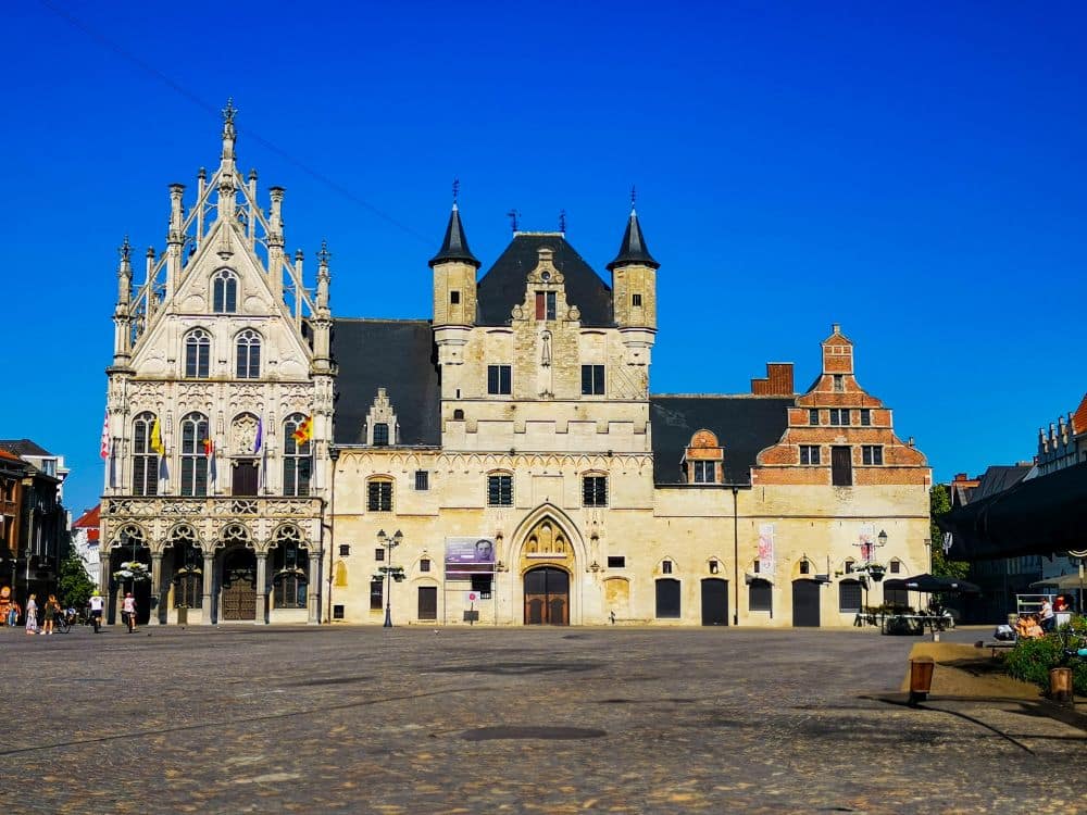 Ein historisches Gebäude mit Elementen aus der Gotik und der Renaissance steht auf einem weitläufigen Kopfsteinpflasterplatz dieser flämischen Stadt. Die kunstvolle Fassade und die Türme bilden eine bezaubernde Kulisse für alle, die eine charmante Übernachtung suchen oder ein Hotel in Mechelen entdecken möchten.