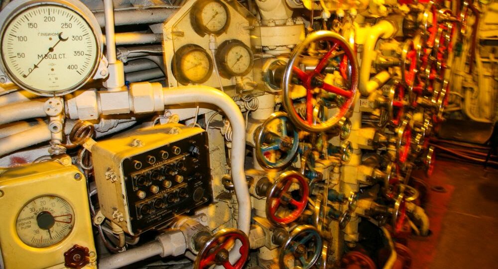 Eine Nahaufnahme einer Schalttafel mit zahlreichen Anzeigen, Zifferblättern, Rohren und Ventilen im Inneren des U-461 im Maritim Museum Peenemünde schafft eine komplexe mechanische Umgebung, die an historische Unterseeboote erinnert.