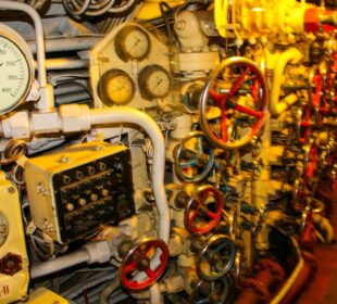 Eine Nahaufnahme einer Schalttafel mit zahlreichen Anzeigen, Zifferblättern, Rohren und Ventilen im Inneren des U-461 im Maritim Museum Peenemünde schafft eine komplexe mechanische Umgebung, die an historische Unterseeboote erinnert.
