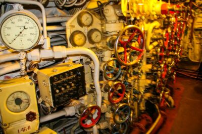 Eine Nahaufnahme einer Schalttafel mit zahlreichen Anzeigen, Zifferblättern, Rohren und Ventilen im Inneren des U-461 im Maritim Museum Peenemünde schafft eine komplexe mechanische Umgebung, die an historische Unterseeboote erinnert.