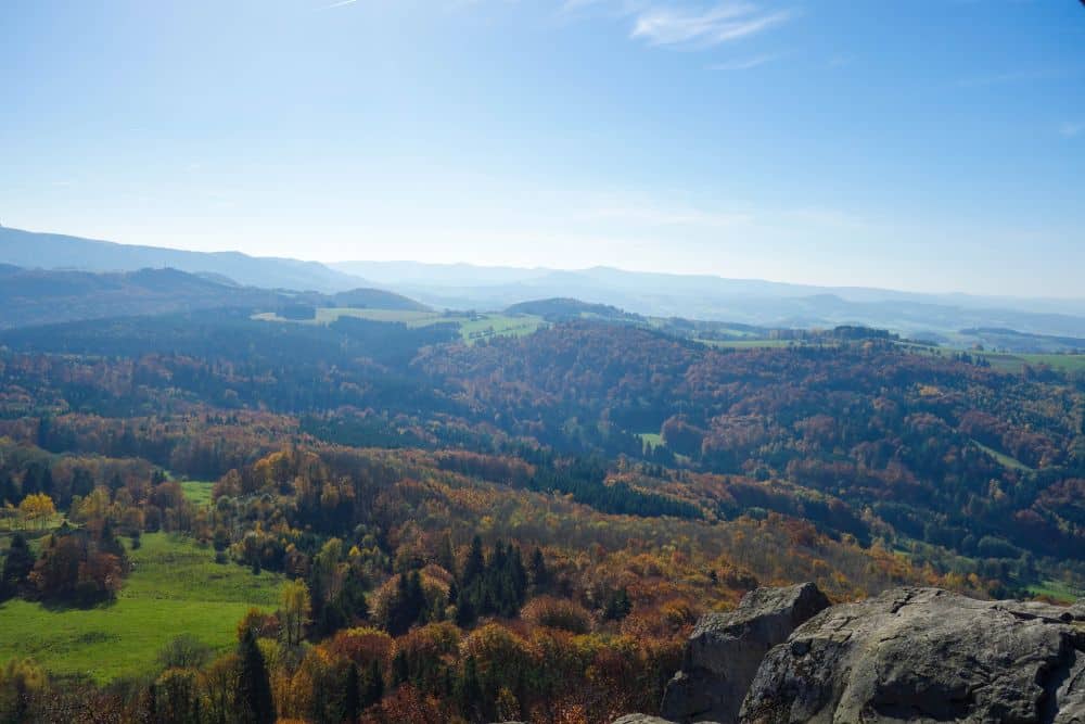 Genießen Sie eine ruhige, malerische Landschaft mit sanften Hügeln in der Rhön, bedeckt mit Herbstlaub, mit der Milseburg in der Ferne, einem klaren blauen Himmel darüber und einem felsigen Vordergrund - perfekt für Ihr nächstes Wanderabenteuer.