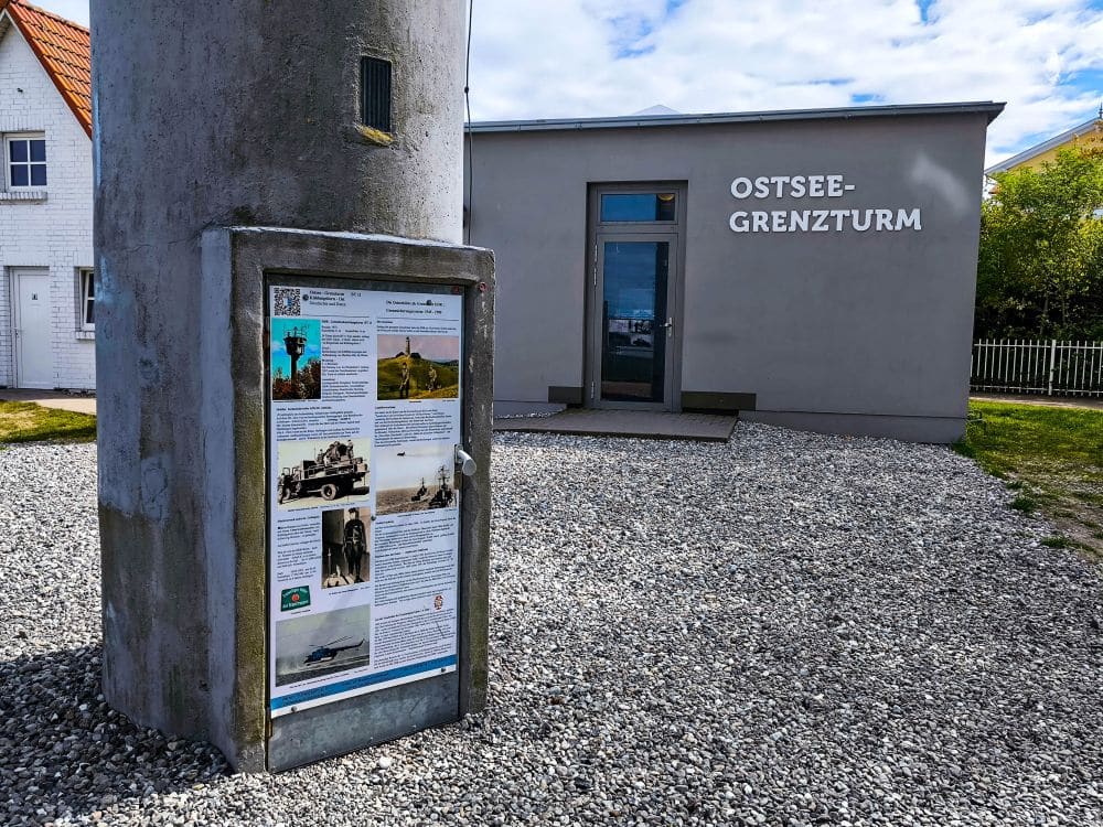 Foto vom Ostsee-Grenzturm-Museum in Kühlungsborn. Im Vordergrund informiert eine Schautafel mit Fotos und Texten über das historische Wahrzeichen der Ostsee, das sich hervorragend für eine kulturelle Auszeit am Meer eignet.