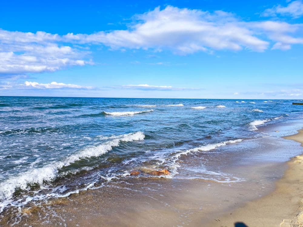 Bei strahlend blauem Ostseehimmel mit vereinzelten Wolken rollen an einem sonnigen Tag die Wellen sanft an den Sandstrand in Kühlungsborn.