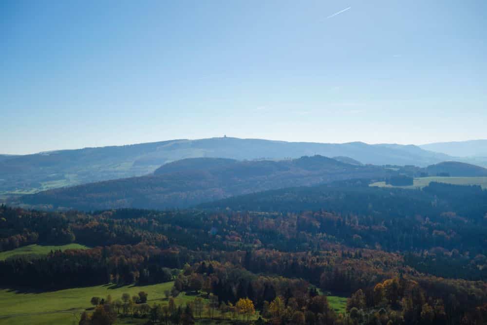 Ein Panoramablick auf die sanfte Hügellandschaft der Rhön mit der Milseburg, auf Wälder und offene Felder unter einem strahlend blauen Himmel - perfekt für ein Wanderabenteuer an einem sonnigen Tag.