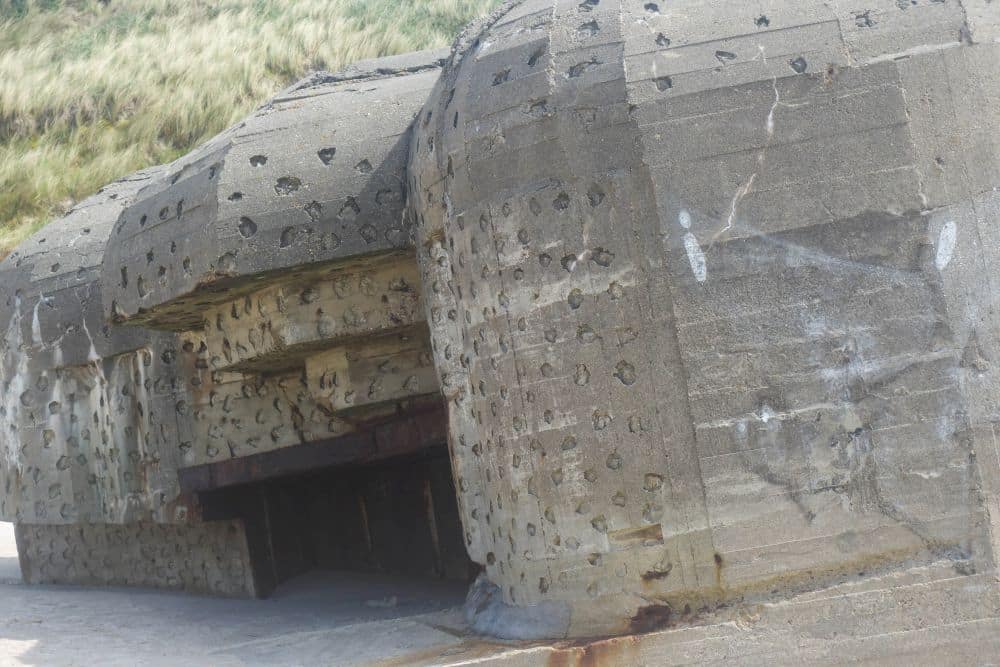 Ein verwitterter Betonbunker aus dem Zweiten Weltkrieg mit vielen Pockennarben und Narben, teilweise im Sand vergraben, liegt am Fuße eines grasbewachsenen Hügels in Dänemarks Westen bei Blavand - ein Zeugnis des wildromantischen Westens.