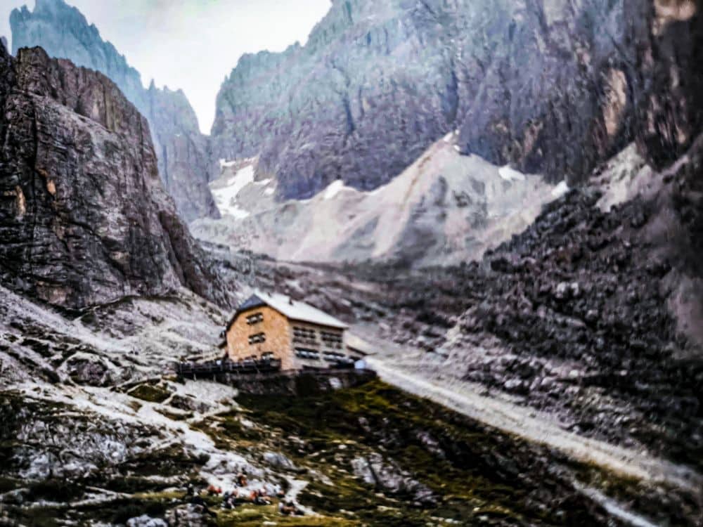 Eine steinerne Berghütte steht an einem grasbewachsenen Hang nahe der berühmten Langkofelscharte, umgeben von steilen, schroffen Felsen in der dramatischen Dolomitenlandschaft - ein echter Klassiker für alpine Abenteurer.