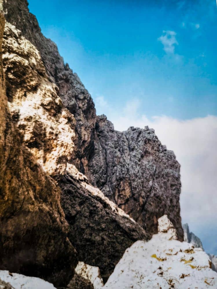 Felsige Bergklippen mit leichtem Schnee am Fuß, unter einem strahlend blauen Himmel mit vereinzelten Wolken - ein ikonischer Anblick des Dolomitenklassikers in der Nähe der Langkofelscharte in den beeindruckenden Dolomiten.