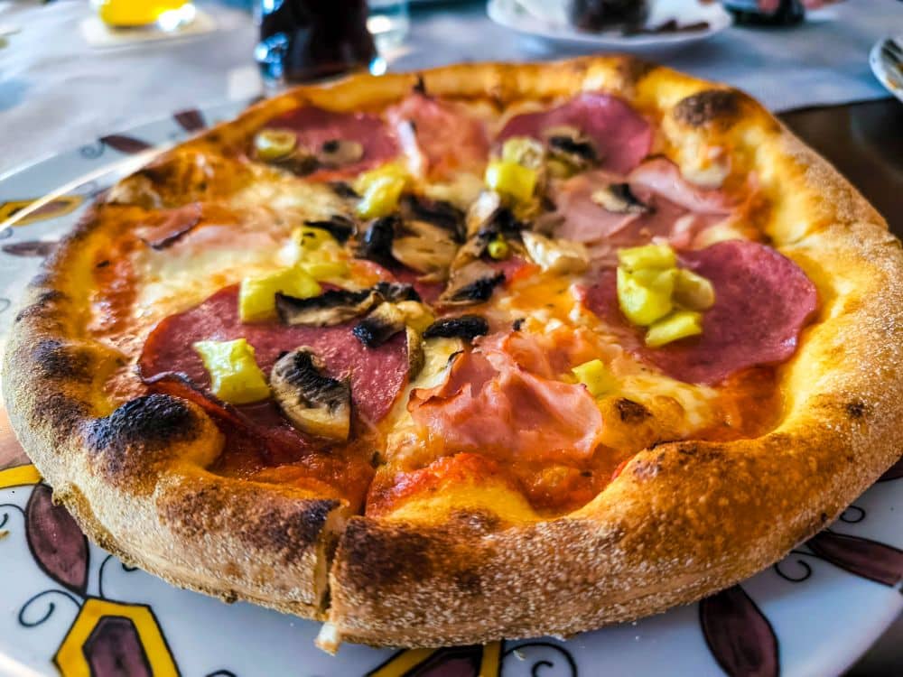 Eine Nahaufnahme einer frisch gebackenen Pizza mit Peperoni, Schinken, Champignons und gelber Paprika auf einem dekorativen Teller in Fulda. Die goldbraune Kruste und der perfekt geschmolzene Käse machen sie unwiderstehlich.