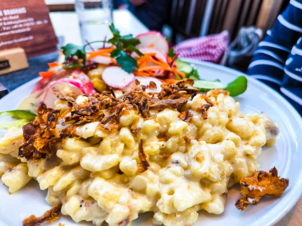 Ein Teller mit cremigen Makkaroni und Käse, überbacken mit knusprigen Röstzwiebeln, serviert mit einem frischen gemischten Salat aus Radieschen, Karotten und Grünzeug - perfekt für eine gemütliche Auszeit in Kühlungsborn.