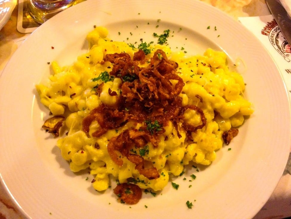 Ein Teller mit Käsespätzle, belegt mit knusprigen Röstzwiebeln und bestreut mit gehackter Petersilie, serviert auf einem weißen Teller - eine klassische Oberstdorfer Spezialität.