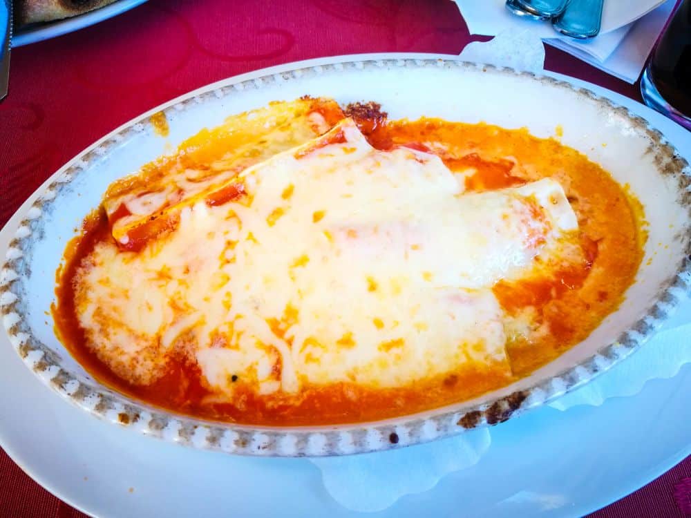 Eine gebackene Käselasagne mit geschmolzenem Käse und Tomatensoße, serviert in einer ovalen Keramikschale auf einem weißen Teller, bringt einen Hauch von Italien auf den Tisch - eine gemütliche Mahlzeit, perfekt für jeden Erfurter Abend.