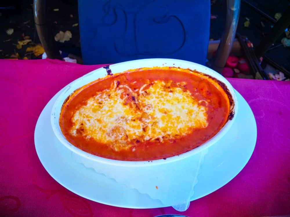 Ovale weiße Schale, gefüllt mit gebackener Lasagne, überbacken mit geschmolzenem Käse und Tomatensoße, auf einem weißen Teller auf einer roten Tischdecke platziert, erinnert an eine gemütliche Trattoria in Erfurt.