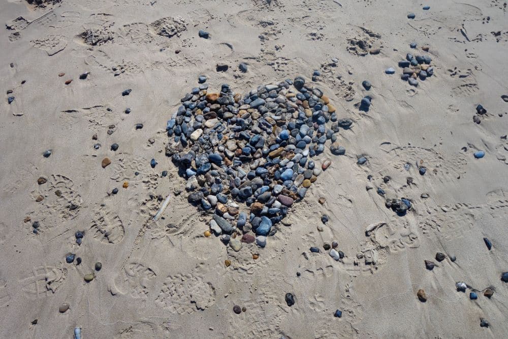 Am Sandstrand von Blavand, Dänemarks wildromantischem Westen, ist eine Herzform aus kleinen Steinen und Kieselsteinen angeordnet, umgeben von Fußspuren und verstreuten Steinen.