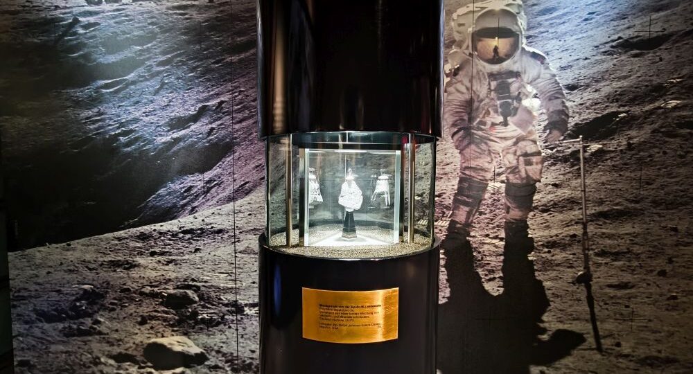 Ein Mondgestein in einer Glasvitrine des Rieskratermuseums mit einem Astronauten auf der Mondoberfläche und einem Lunar Rover in der Ferne verdeutlicht die einzigartige Verbindung Nördlingens zur geologischen Geschichte der Schwäbischen Alb.