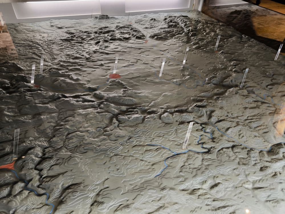 Eine detaillierte topografische 3D-Reliefkarte zeigt Berge, Täler und Flüsse der Schwäbischen Alb, mit mehreren transparenten vertikalen Markierungen, die wichtige Orte in der Nähe von Nördlingen und dem berühmten Rieskratermuseum hervorheben.