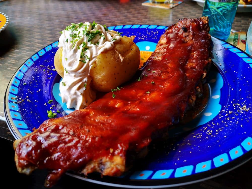 Ein Teller mit gegrillten Rippchen in Soße, dazu zwei Bratkartoffeln mit Sauerrahm und Kräutern - ein Gericht, das man in den Top-Restaurants auf der schönen Insel Rügen findet.