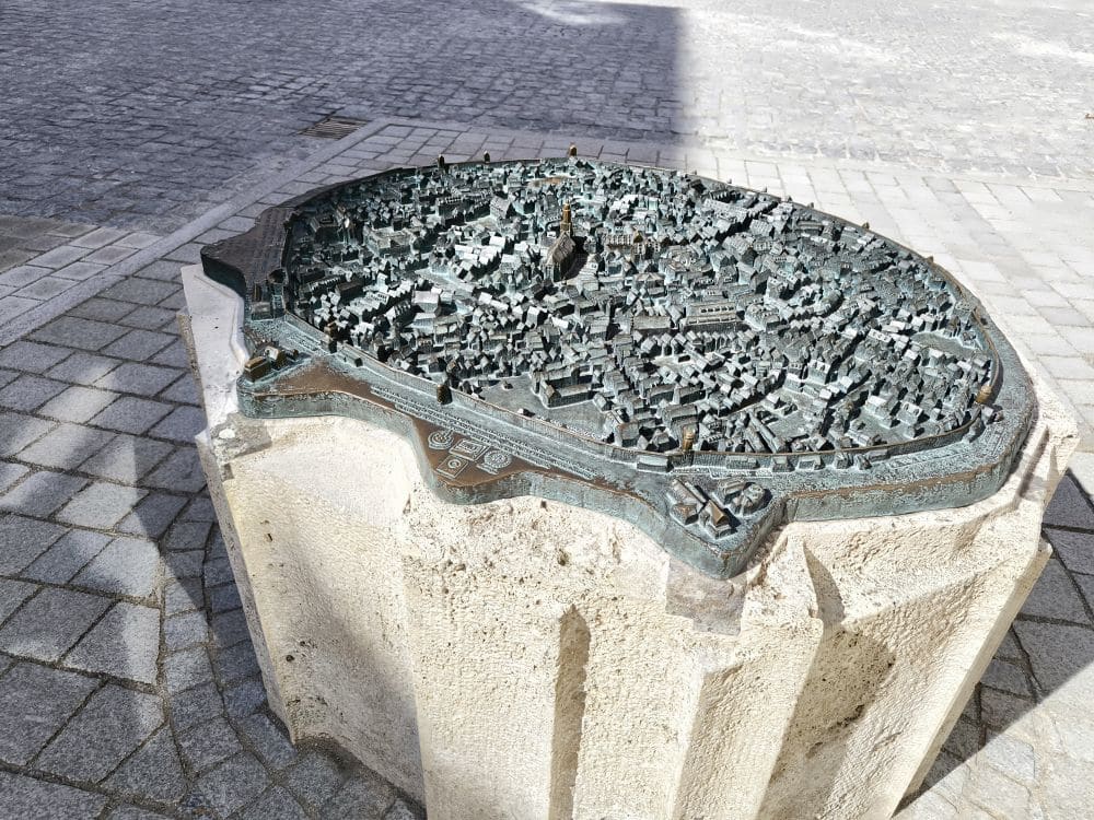Ein taktiles Bronzemodell von Nördlingen steht auf einem Steinsockel auf einem Kopfsteinpflaster und zeigt detaillierte Gebäude und Straßen, die der Besucher durch Berührung erkunden kann.