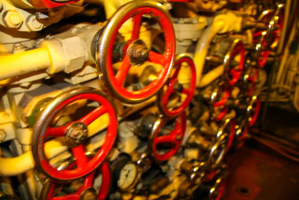 Nahaufnahme mehrerer roter und silberner Metall-Ventilräder, die an gelben Rohren und Maschinen befestigt sind, wahrscheinlich Teil eines Motors oder eines industriellen Steuerungssystems, das an die in Peenemünde entwickelte Technologie erinnert.