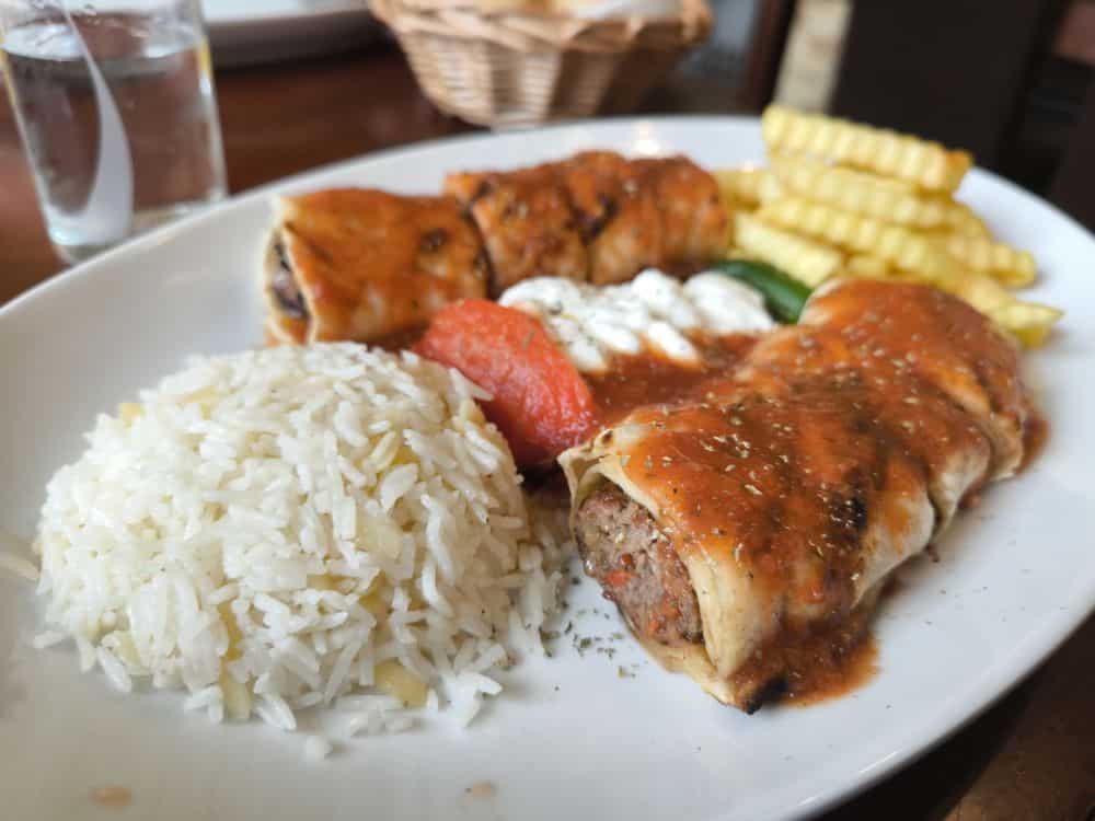 Ein Teller mit Reis, zwei mit Fleisch gefüllten Brötchen mit Tomatensoße, Pommes frites, einer Scheibe Tomate und weißer Soße - typisch für die deftigen Gerichte des Lieblingsrestaurants Rügen auf der schönen Insel Rügen.