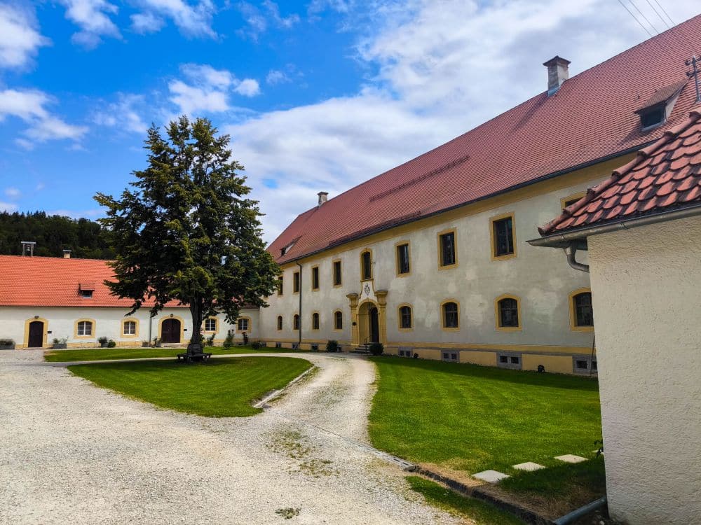 In der Nähe von Hayingen steht ein großes historisches Gebäude mit rotem Ziegeldach, cremefarbenen Wänden und gelben Fensterrahmen, umgeben von einem gepflegten Rasen und geschwungenen Kieswegen - ein perfekter Anblick auf Ihrer Wanderung Glastal bei teilweise bewölktem blauen Himmel.