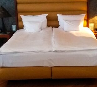 Ein ordentlich gemachtes Doppelbett mit weißer Bettwäsche und zwei Kissen, umrahmt von einem braunen gepolsterten Kopfteil - perfekt für die Übernachtung in München. Die Nachttische auf beiden Seiten bieten jeweils eine Lampe und ein Telefon für Ihren Komfort.