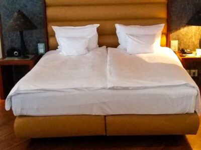 Ein ordentlich gemachtes Doppelbett mit weißer Bettwäsche und zwei Kissen, umrahmt von einem braunen gepolsterten Kopfteil - perfekt für die Übernachtung in München. Die Nachttische auf beiden Seiten bieten jeweils eine Lampe und ein Telefon für Ihren Komfort.