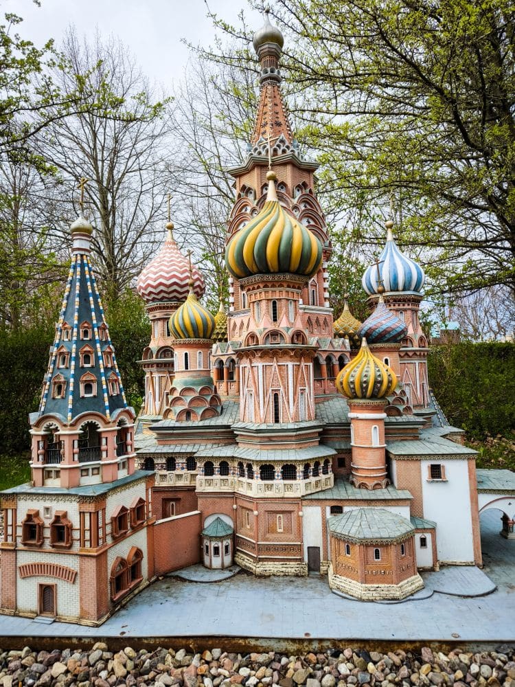 Ein detailgetreues Miniaturmodell der Basilius-Kathedrale mit bunten Zwiebeltürmen, das im Freien auf einem felsigen Sockel inmitten von Bäumen und Grün im Rügenpark steht.