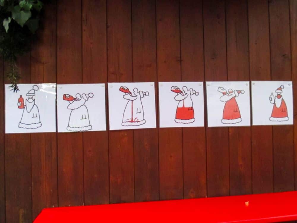 Sechs aufeinanderfolgende Zeichnungen einer Frau mit Haube, die einen Becher hält, die nach und nach mit mehr Farbe gefüllt werden, ergeben eine festliche Weihnachtsszene auf einer Holzwand über einer roten Fläche.