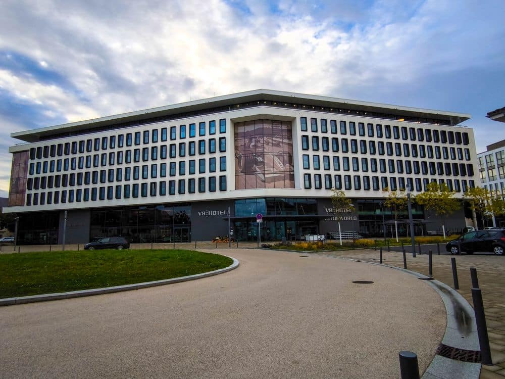 Ein modernes, mehrstöckiges Hotelgebäude in Böblingen mit gleichmäßig verteilten Fenstern und einem großen Glaseingang ist umgeben von einer Einfahrt, kleinen Bäumen und geparkten Autos unter einem bewölkten Himmel.