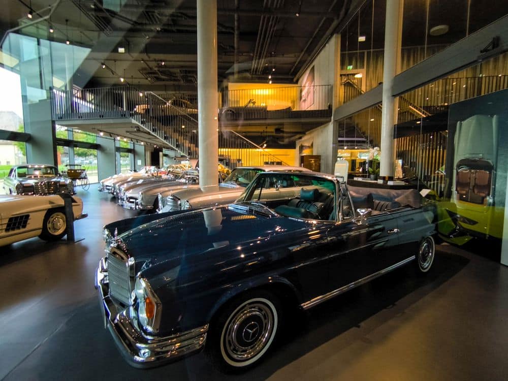 Ein klassisches dunkelblaues Cabriolet ist in einem modernen, geräumigen Böblinger Automuseum mit Glaswänden und mehreren Oldtimern im Hintergrund ausgestellt.