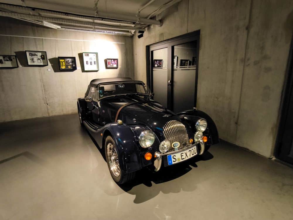 Ein klassischer schwarzer Oldtimer mit Chromakzenten steht in einem modernen Raum mit Betonwänden in Böblingen, mit gerahmten Fotos an der Wand und sanfter Deckenbeleuchtung.