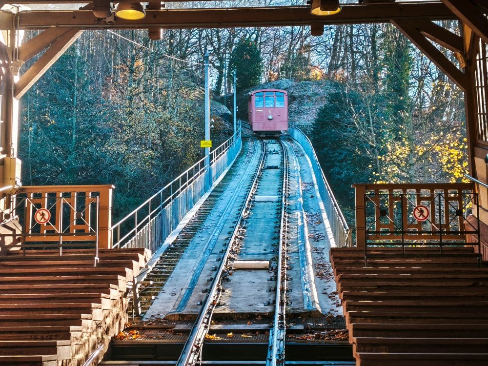 In der Nähe des Heidelberger Schlosses führt eine rote Standseilbahn über eine steile Strecke durch ein Waldgebiet. Von einer überdachten Station mit Holzbänken und Sicherheitsschildern aus kann man die romantischste Ruine Reise beginnen.